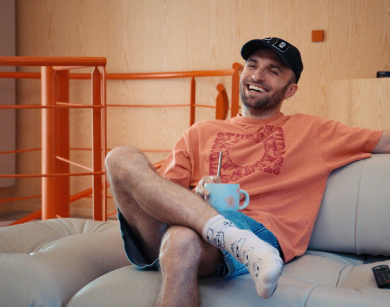 Squeezie qui sourit avec les jambes croisées et une tasse à la main